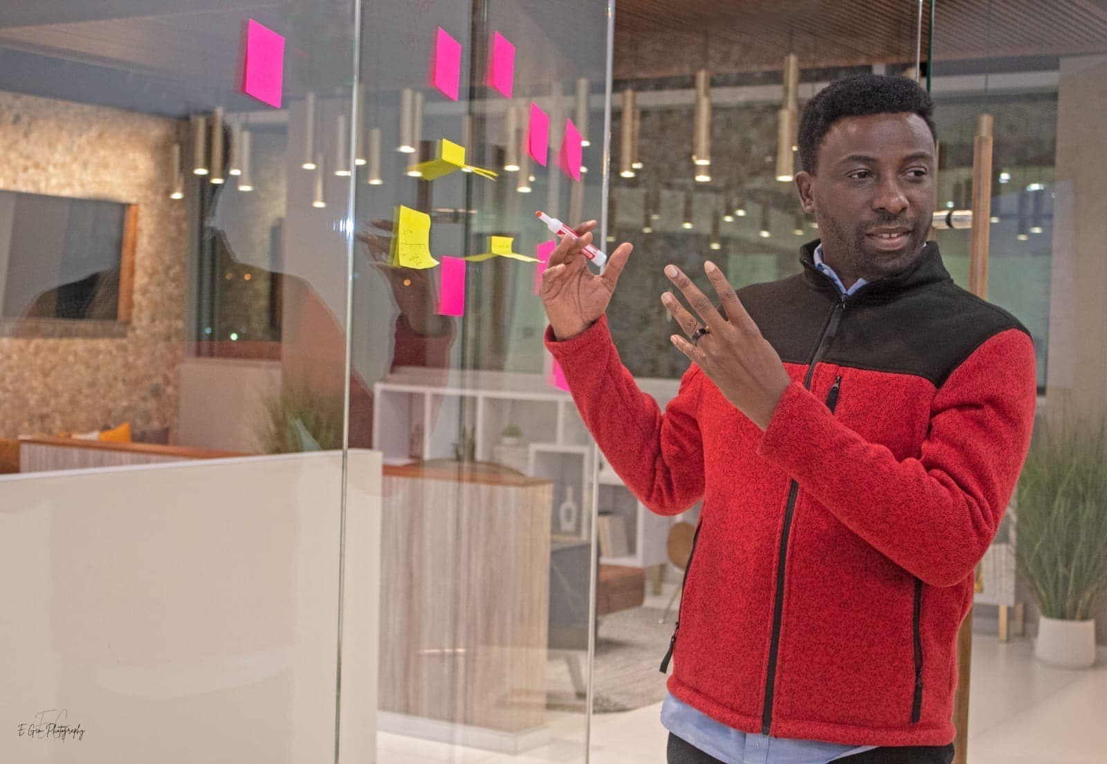 Divine Oshideko facilitating beside a glass wall covered with workshop notes